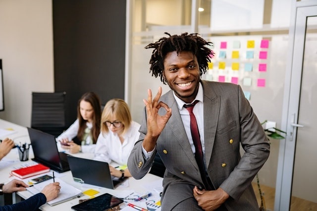Employee giving the okay sign with hand with coworkers working in the background